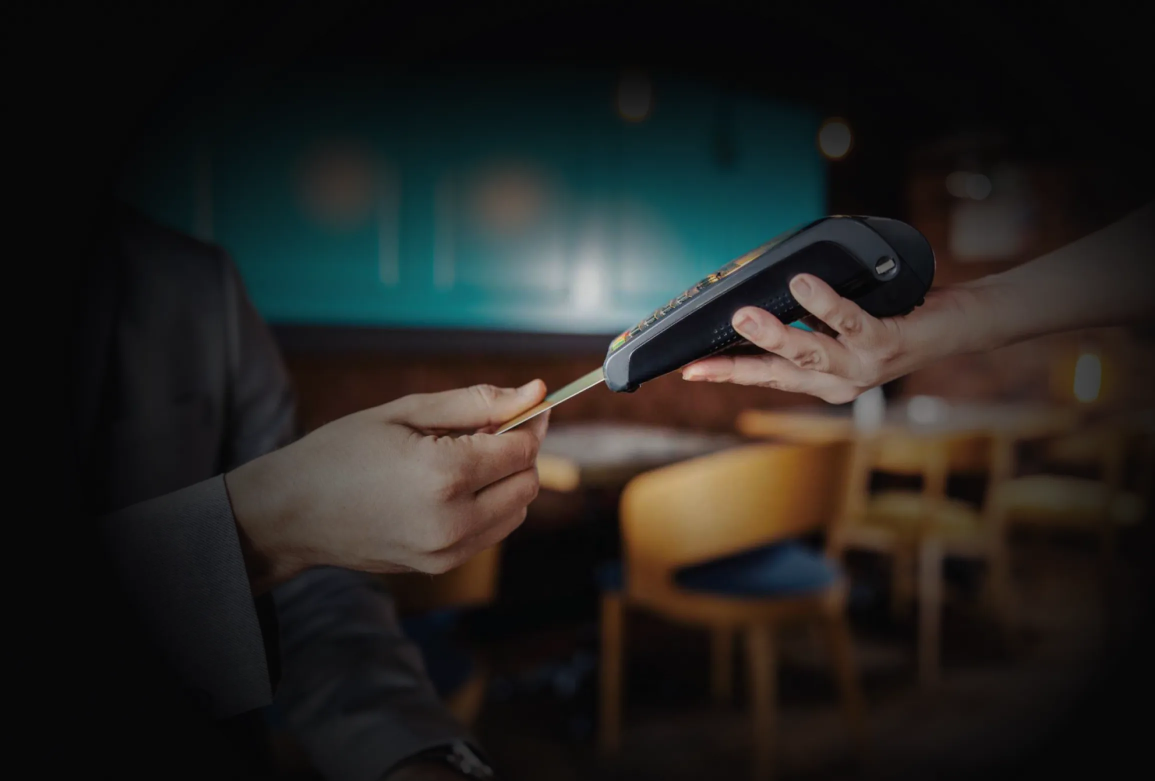 Hand paying by card at a countertop payment terminal in a warm-lit restaurant