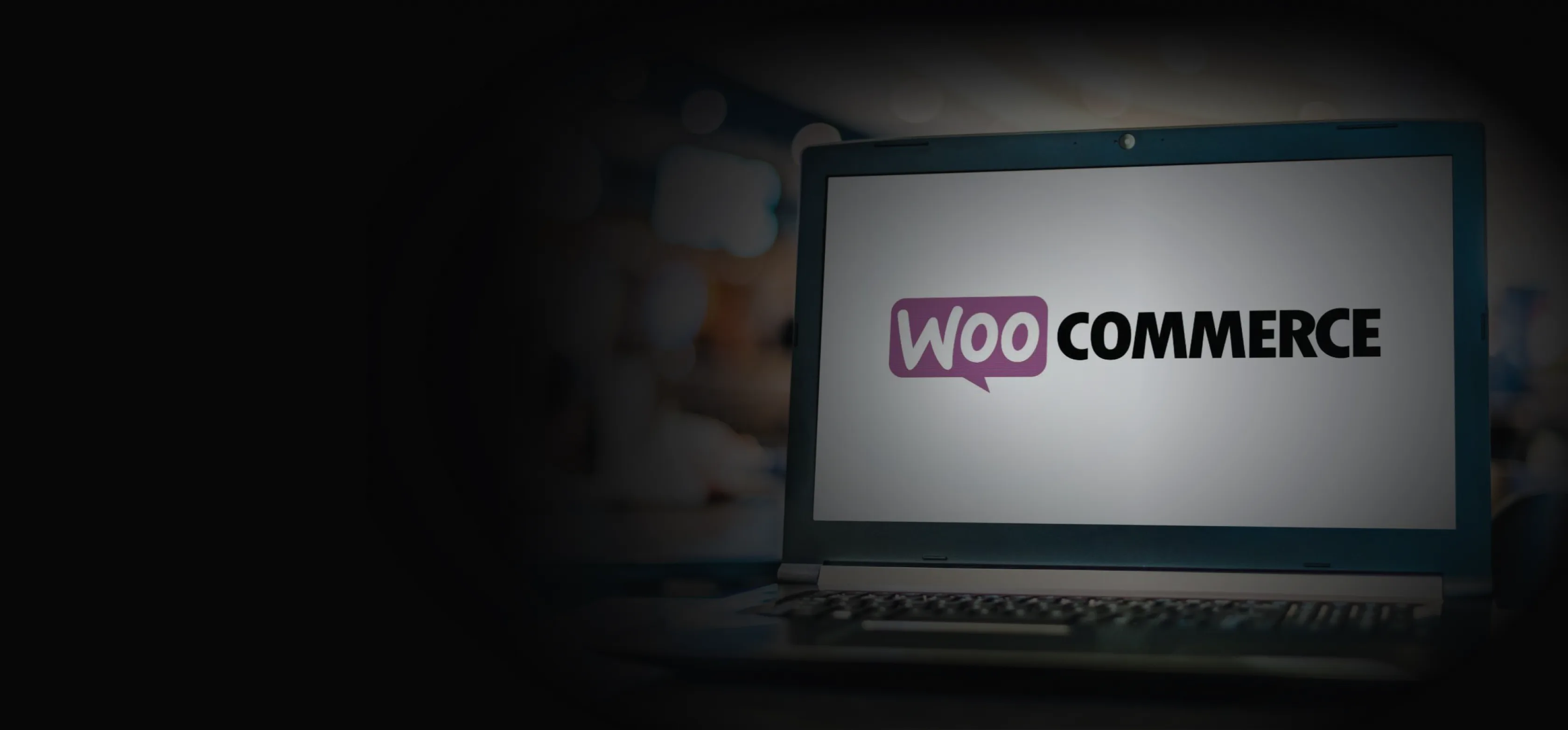 Laptop displaying the WooCommerce logo, fading into the dark section background