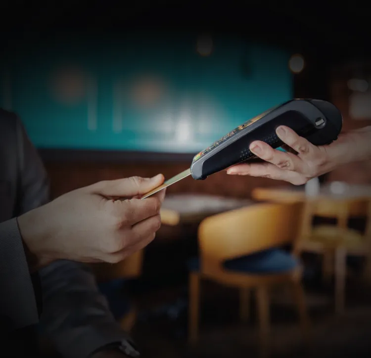Hand paying by card at a countertop payment terminal in a warm-lit restaurant